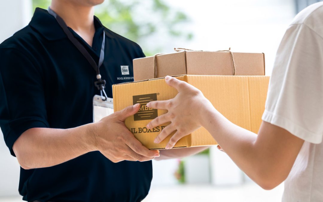 Delivery person in a dark polo hands two bundled cardboard boxes to a customer wearing a white shirt.